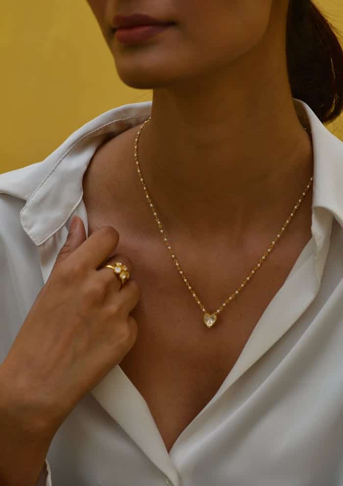 pexels-photo-17298621 Close-up of a woman displaying a heart-shaped pendant and elegant ring against a yellow backdrop.